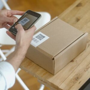 A person uses a smartphone to scan a QR code on a package in an online store setting.